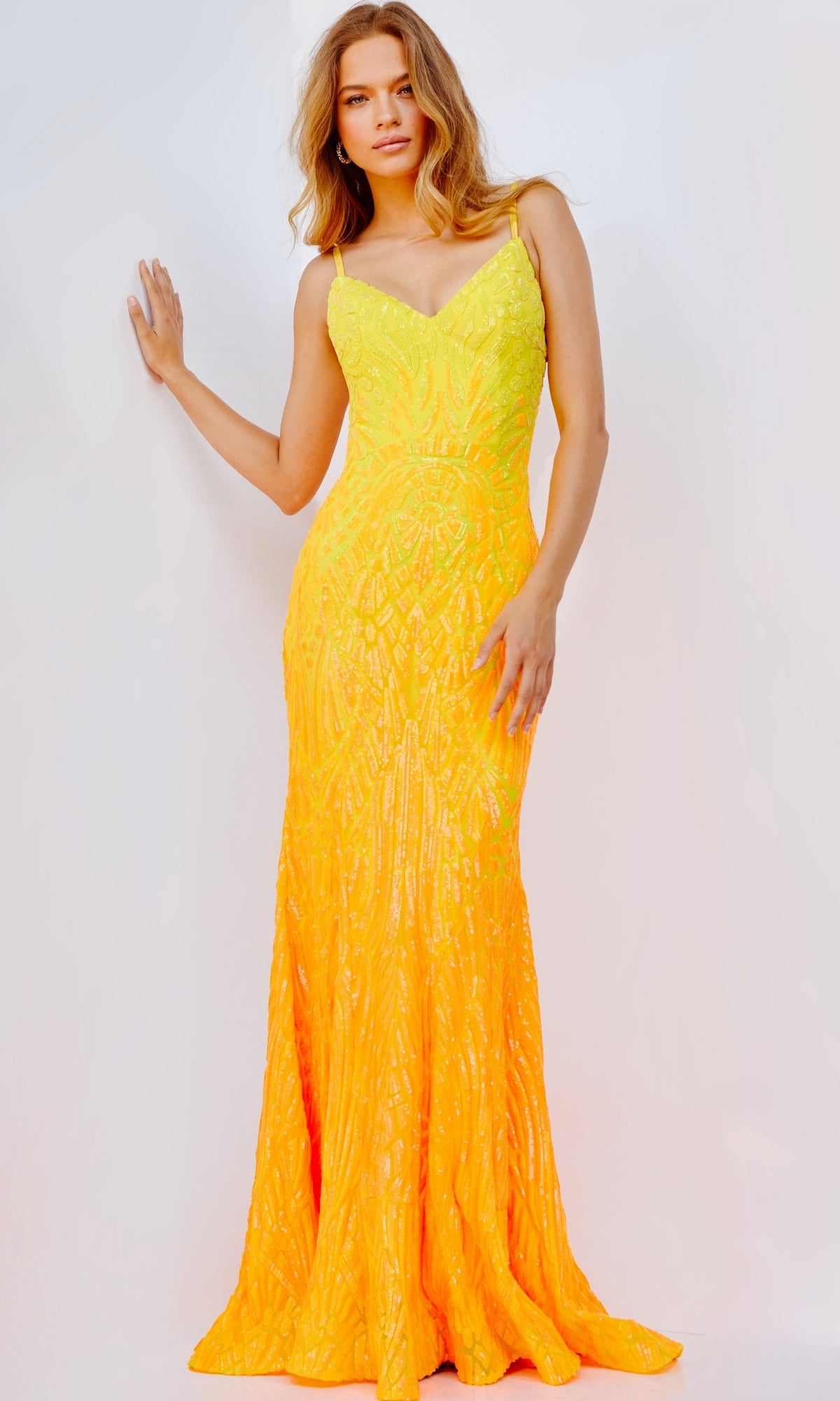 A woman poses against a plain light background wearing the Jovani 06450 Sequin-Print Long Prom Dress in yellow/orange, featuring a sleeveless fitted silhouette, open back, and intricate sequin detailing.